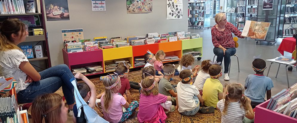 Les enfants assis par terre et bibliothécaire assis sur une chaise avec un livre.
