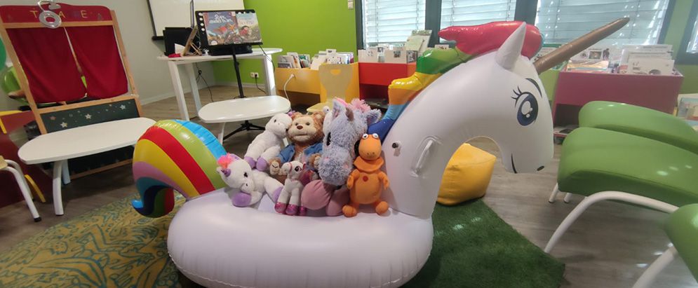 Une photo : l'interieur de la médiathèque, un grand licorne gonflable et des peluches.